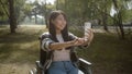A pretty disabled asian girl with long dark hair, sitting in a wheelchair in the public park, stops talking to her