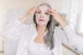 Pretty elderly gray haired woman puts cloth nourishing mask on her face skin for rejuvenating and eliminating defects