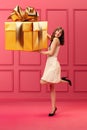 Pretty, elegant young girl holding giant golden present box, Christmas gift against pink background. Happiness, surprise Royalty Free Stock Photo