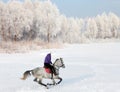 Pretty equestrian girl riding her black horse through snow outdoors Royalty Free Stock Photo