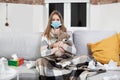 Pretty exhausted sick teen girl in medical mask, sitting on soft sofa in living-room at home, covered with plaid and Royalty Free Stock Photo
