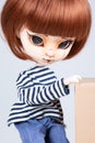 Pretty expressive doll with big eyes red hairs in blue shirt hand on carton box in white background