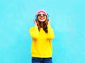 Pretty fashion cool smiling girl listening to music in headphones wearing a colorful pink hat, yellow sunglasses and sweater Royalty Free Stock Photo