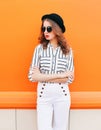 Pretty fashion woman model wearing black hat sunglasses white pants over colorful orange background Royalty Free Stock Photo