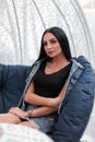 Pretty fashionable beautiful young brunette woman in a stylish denim jacket in a T-shirt resting sitting on a vintage soft chair Royalty Free Stock Photo