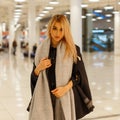 Pretty fashionable beautiful young woman blonde in a stylish autumn coat with a vintage scarf doing shopping in a mall. Royalty Free Stock Photo