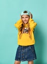 Funny teenage girl in a baseball cap and yellow hoodie covered her ears with her hands on a blue background. Royalty Free Stock Photo