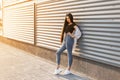 Pretty fashionable young woman in blue jeans in white sneakers in a stylish top in a summer jacket with long hair poses