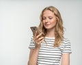 Pretty female checking social media on mobile phone standing near white wall, gray background Royalty Free Stock Photo