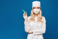 Pretty female doctor wearing white medical robe holding syringe at blue background, isolated. Healthcare and Royalty Free Stock Photo