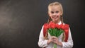 Pretty female first-grader holding tulips bouquet against blackboard background