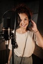 Pretty female singer in headphones happily looking in camera working on new music album in recording studio Royalty Free Stock Photo