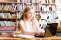 Pretty female student typing on notebook in library Royalty Free Stock Photo