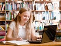 Pretty female student typing on notebook in library Royalty Free Stock Photo