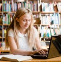 Pretty female student typing on notebook in library Royalty Free Stock Photo
