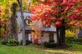 Pretty field stone house with steep metal roof nestled among trees with colourful foliage