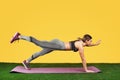 Pretty fit young woman do exercise on the fitness purple mat on green grass over yellow background.