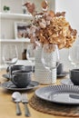 Pretty flowers in vase on a dinning table with served dishware