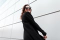 Pretty funny beautiful hipster woman in stylish sunglasses in a vintage long black coat with a positive smile poses and laughs