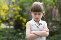 Pretty funny moody little blond preschool girl in white sleeveless dress looks into camera feeling angry and unsatisfied on