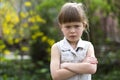 Pretty funny moody little blond preschool girl in white sleeveless dress looks into camera feeling angry and unsatisfied on blurre