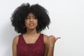 The pretty girl with afro hair points her thumb to the right side in the copy space, announces the product, red colored dress .  Y Royalty Free Stock Photo