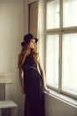 Pretty girl in hat and dress at chair and window