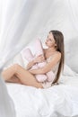 Pretty girl with a beauty pillow in her hands sits in bed and is sad. Vertical photo Royalty Free Stock Photo