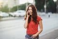 Pretty girl in casual dress is talking on a mobile phone while walking at the city street on a sunset time.