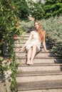 Pretty girl in casual white dress sitting on the stairs in the park.
