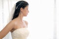Pretty girl dressed in the wedding dress standing by a window with white curtains looking outside pensively on her wedding day. Hi Royalty Free Stock Photo