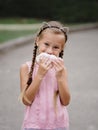 A pretty girl is eating a cheeseburger on a blurred street background. A little girl with a sandwich. Royalty Free Stock Photo