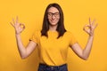 Pretty girl feel relaxed and makes yoga sign with fingers on yellow background