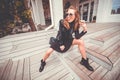 Pretty girl in glam rock style wear sitting on a steps, drinking street coffee and fooling. Showing tongue Royalty Free Stock Photo