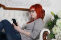 Pretty girl sits on white sofa with smartphone Royalty Free Stock Photo