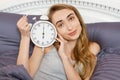 Pretty girl holds a clock and lies in bed bedroom. Emotional beautiful woman lying in bed on her day off Royalty Free Stock Photo