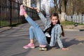 Pretty girl in jeans and pink sneakers sits on a penny board and does exercises. International Skateboarding Day.