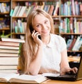 Pretty girl in library typing on laptop and talking on the phone Royalty Free Stock Photo