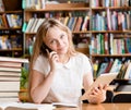 Pretty girl in library using tablet computer and talking on the phone Royalty Free Stock Photo