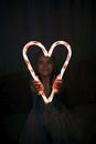 Girl holding big luminous heart over dark background, waiting for love in Valentine Day