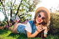 Pretty girl with long curly hair in hat is lying on grass in summer park. on sunlight. She wears jeans jerkin, short Royalty Free Stock Photo