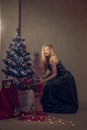Pretty girl in long evening dress near christmas tree taking box with gift Royalty Free Stock Photo