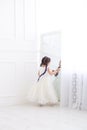 Vertical portrait of a five year old girl in a white dress standing in front of a mirror in a white studio Royalty Free Stock Photo