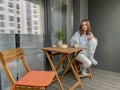 Pretty girl in pajama having breakfast and drinking coffee on balcony or terrace in the morning in city Royalty Free Stock Photo