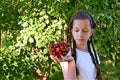 pretty girl with pigtails in a white T-shirt is standing in the garden and holding a glass vase with red, ripe cherries Royalty Free Stock Photo