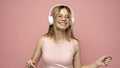 Pretty girl in a pink t-shirt and glasses listening music with her headphones and dancing on pink background. Royalty Free Stock Photo