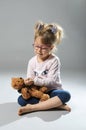 Pretty girl plays in the doctor treats a teddy bear on a gray ba Royalty Free Stock Photo