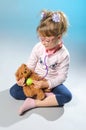 Pretty girl plays in the doctor treats a teddy bear on a gray ba Royalty Free Stock Photo