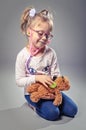 Pretty girl plays in the doctor treats a teddy bear on a gray ba Royalty Free Stock Photo