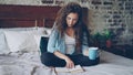 Pretty girl reading book sitting on bed at home and holding cup with drink enjoying free time and resting. Young people Royalty Free Stock Photo